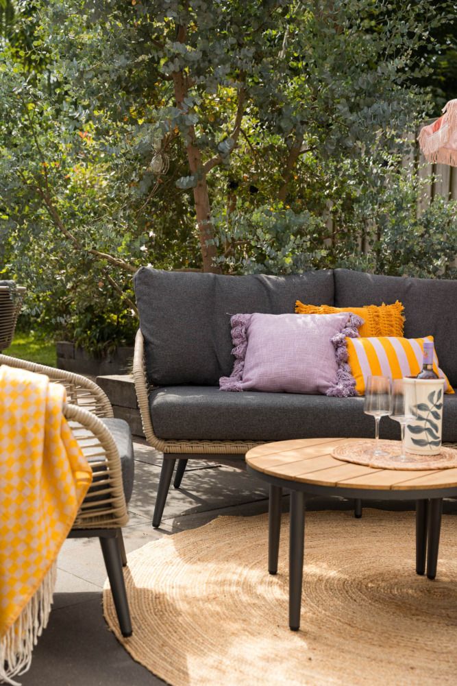 Vooraanzicht van een natuurlijke tuin met een bohemian tuinstijl, voorzien van een aluminium hoek loungeset met loungetafel. 