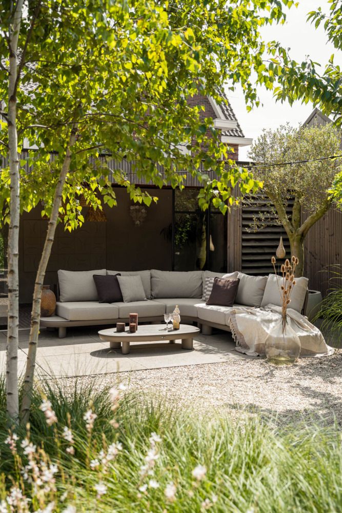 Vooraanzicht van een pergola aan huis met een japandi tuinstijl, voorzien van een houten ronde tuintafel en rope tuinstoelen.