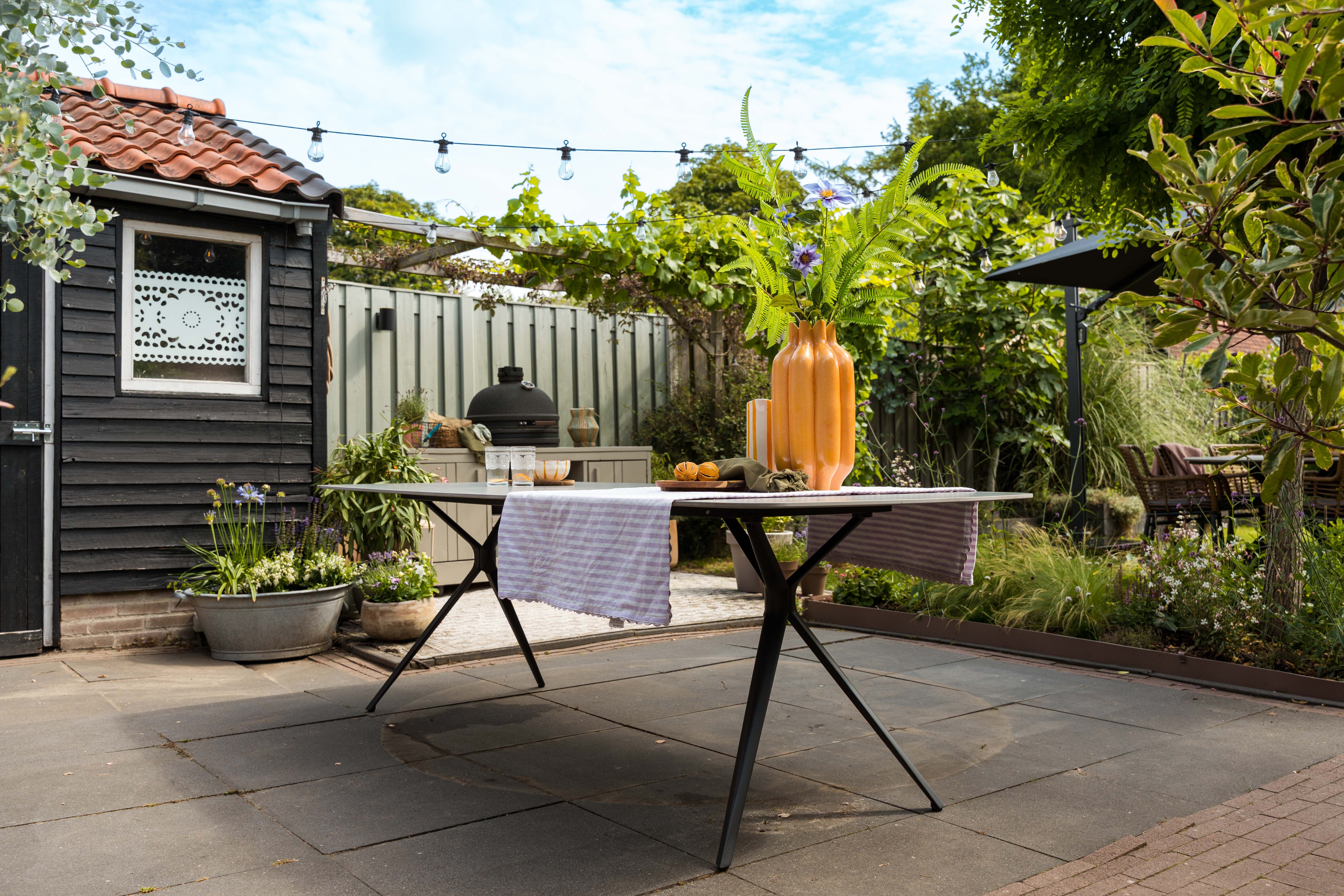 Moderne rechthoekige tuintafel met zwart design onderstel op een sfeervol terras met houten tuinhuis.