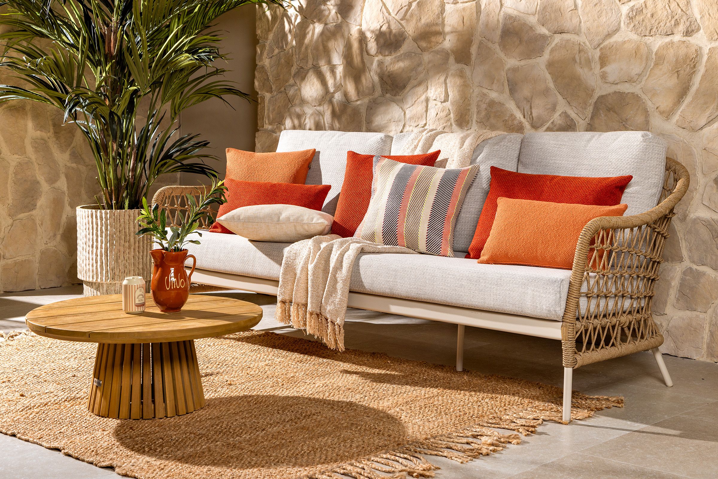 Luxe wicker loungebank met oranje en beige kussens, gecombineerd met een ronde houten loungetafel op een mediterraan terras.