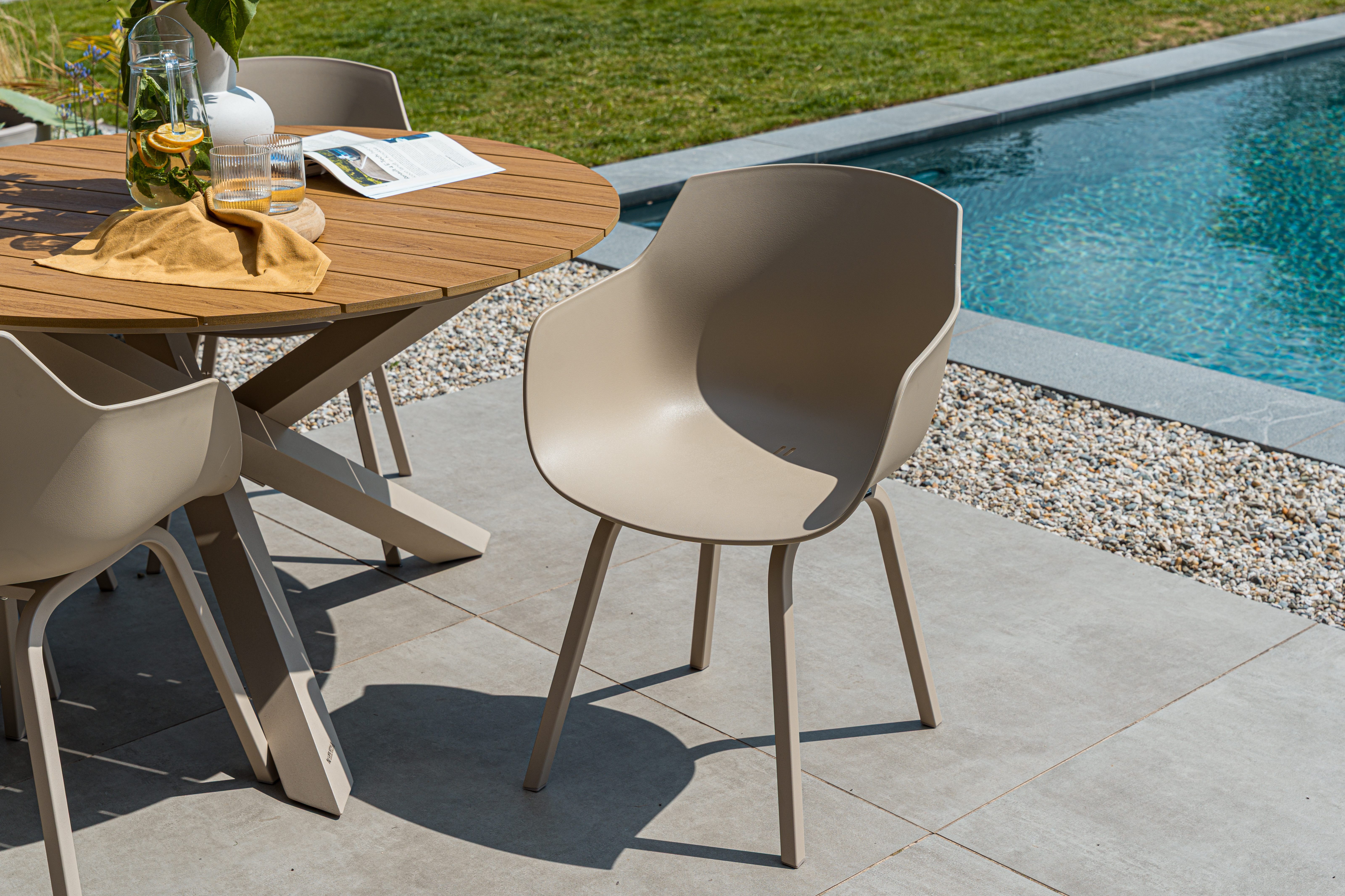 Moderne beige tuinstoelen die perfect passen bij een ronde houten tuintafel op een terras bij het zwembad