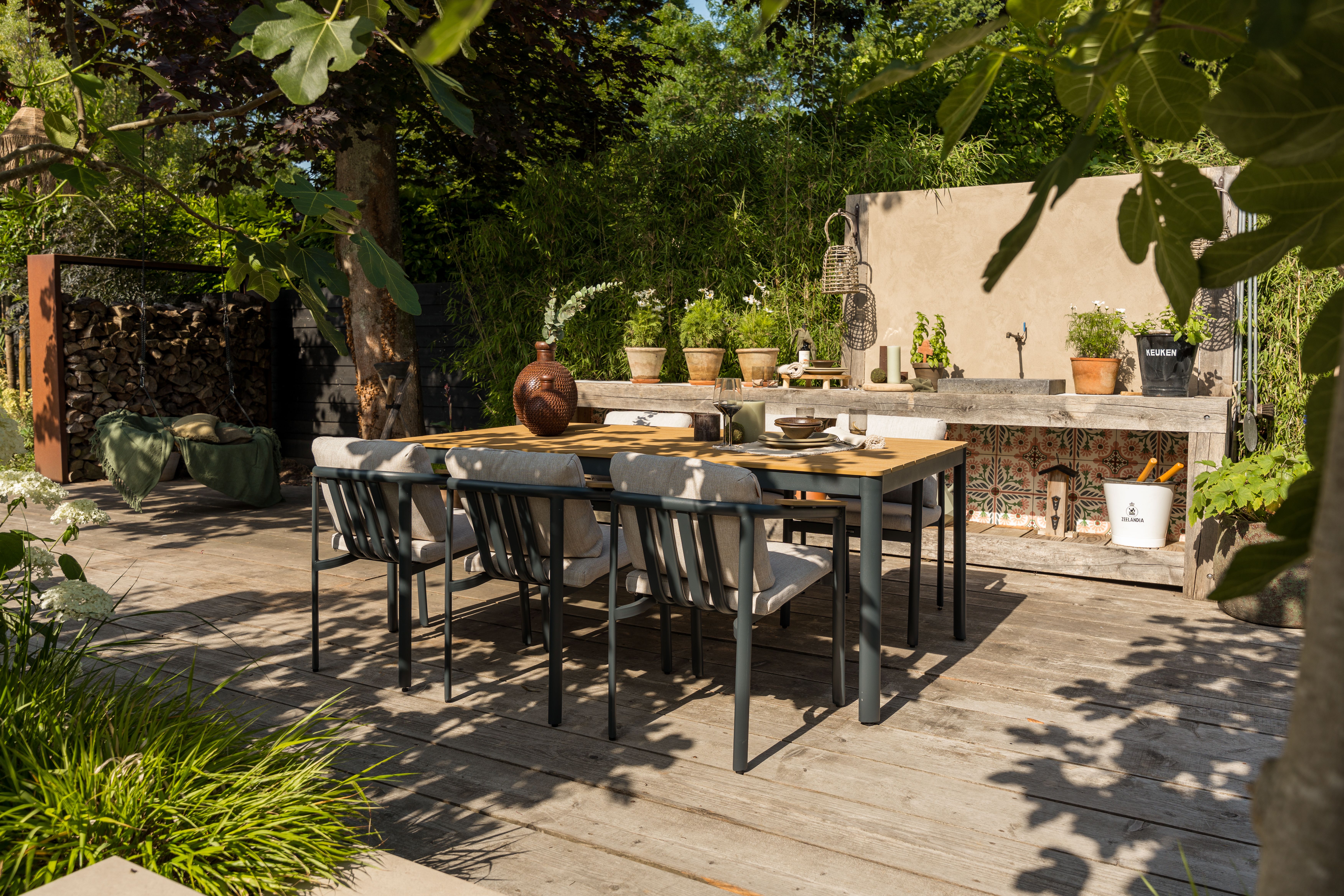 Een moderne tuintafel met strakke en minimalistische tuinstoelen op een terras bij een robuuste buitenkeuken in de tuin.
