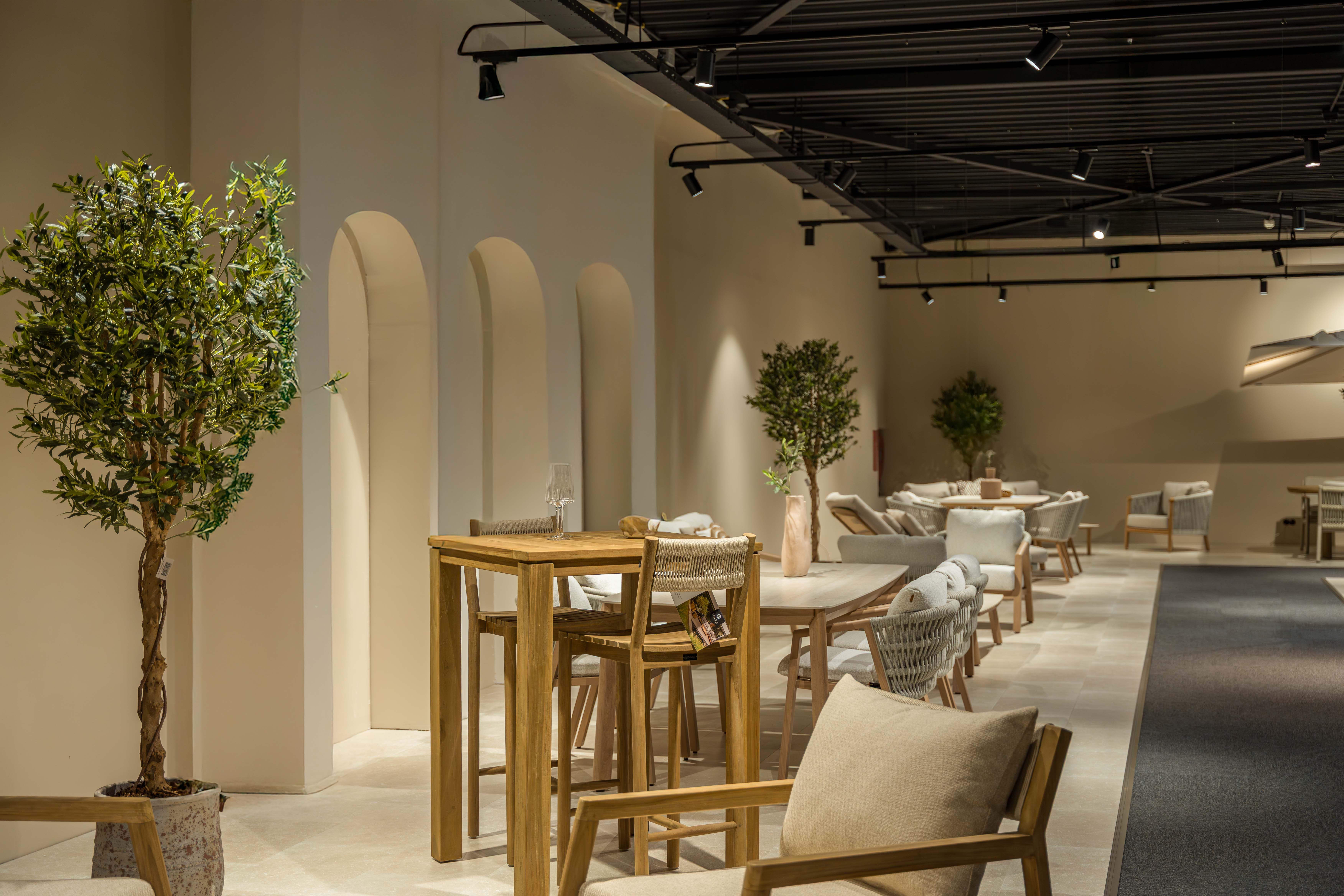 Showroom met moderne houten bartafel en stoelen, beige wanden met boogvormige nissen, sfeerverlichting en stijlvolle interieurdecoratie.