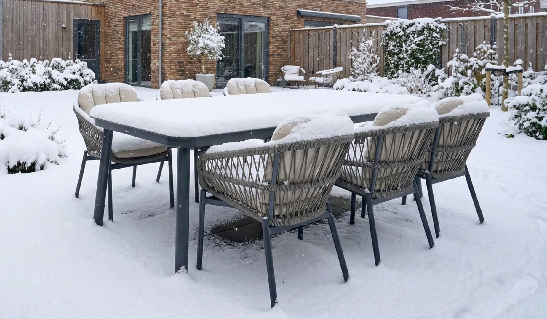 Tuinset met rechthoekige aluminium tuintafel en rope tuinstoelen, bedekt met sneeuw in een winterse tuin.