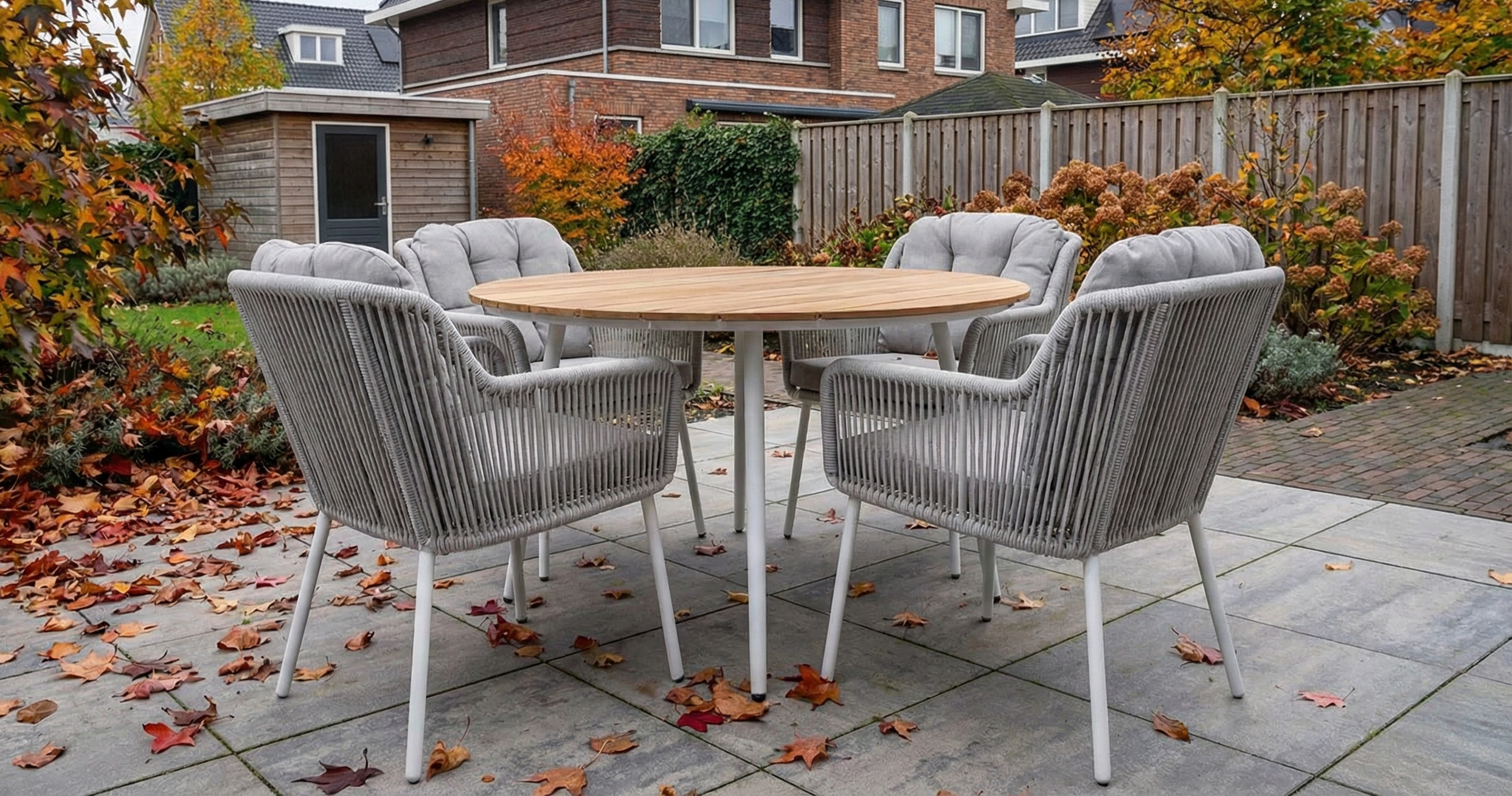 Tuinset met een ronde polywood tuintafel en vier rope tuinstoelen met lichte kussens, geplaatst op een terras in de tuin, omringd door herfstbladeren en warme herfstkleuren.