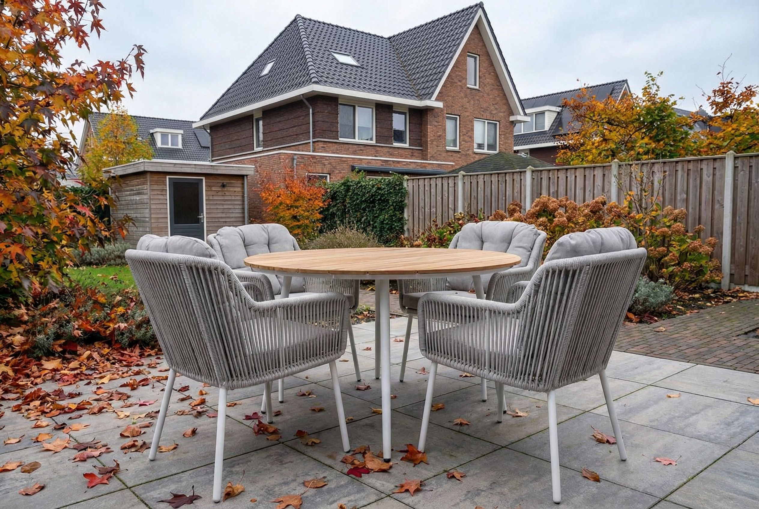 Tuinset met ronde tafel en gevlochten stoelen in achtertuin, met herfstachtig weer en vallende bladeren.