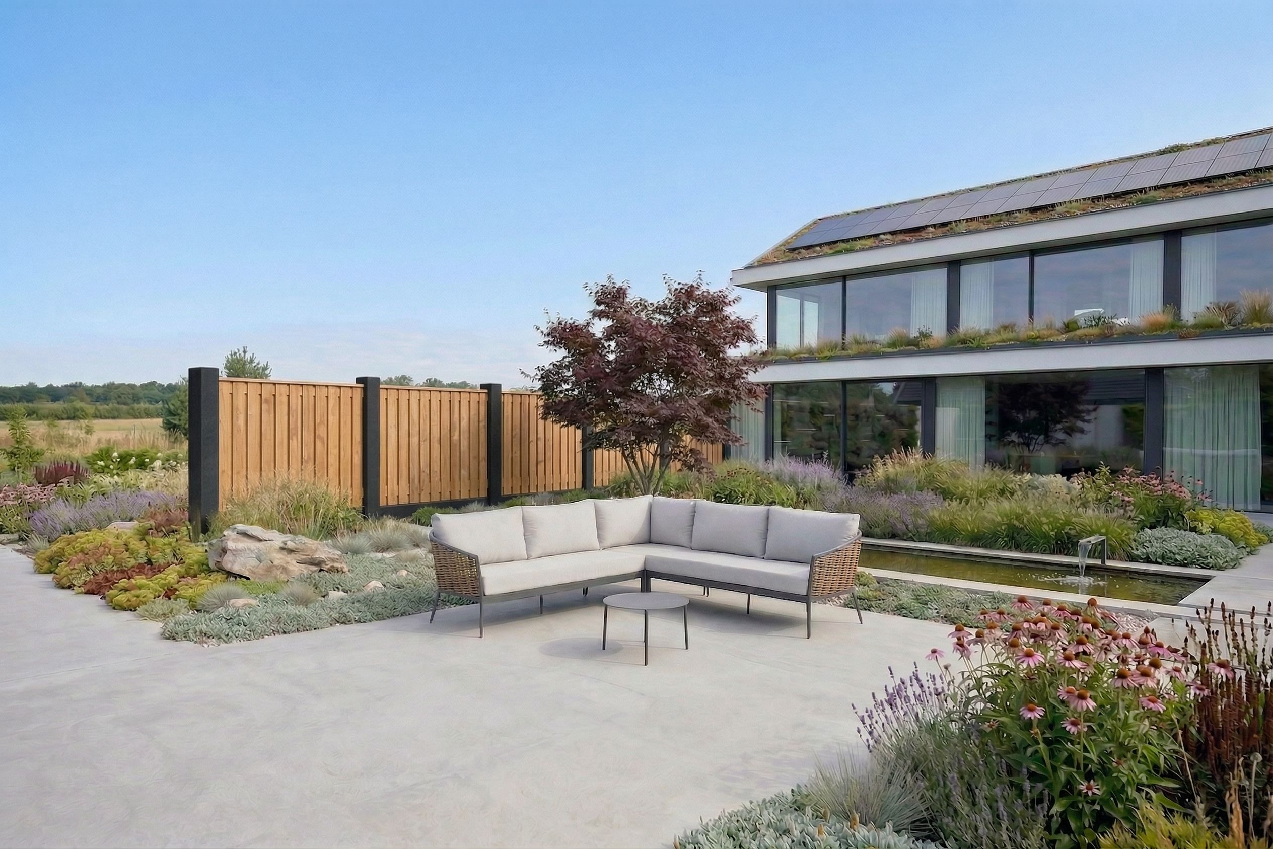 Moderne wicker tuinset met zes tuinstoelen op een strak betegeld terras, geplaatst voor een lichte houten schutting met groene beplanting en een grote terracotta bloempot.