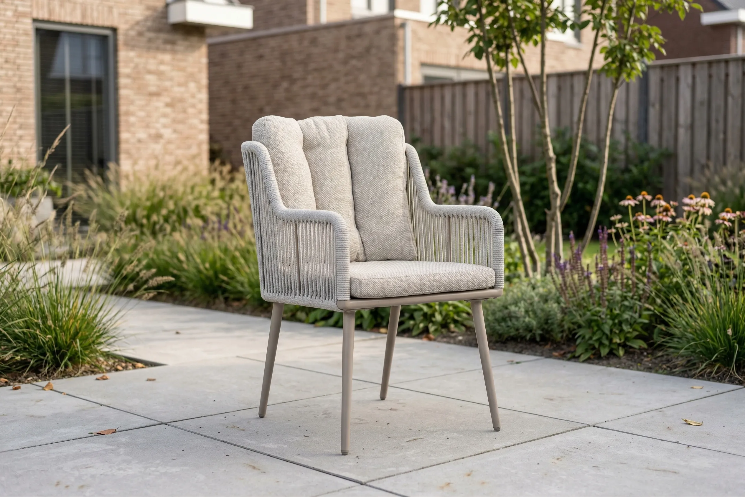 Moderne grijze rope tuinstoel met dikke kussens op een betegeld terras in een tuin.