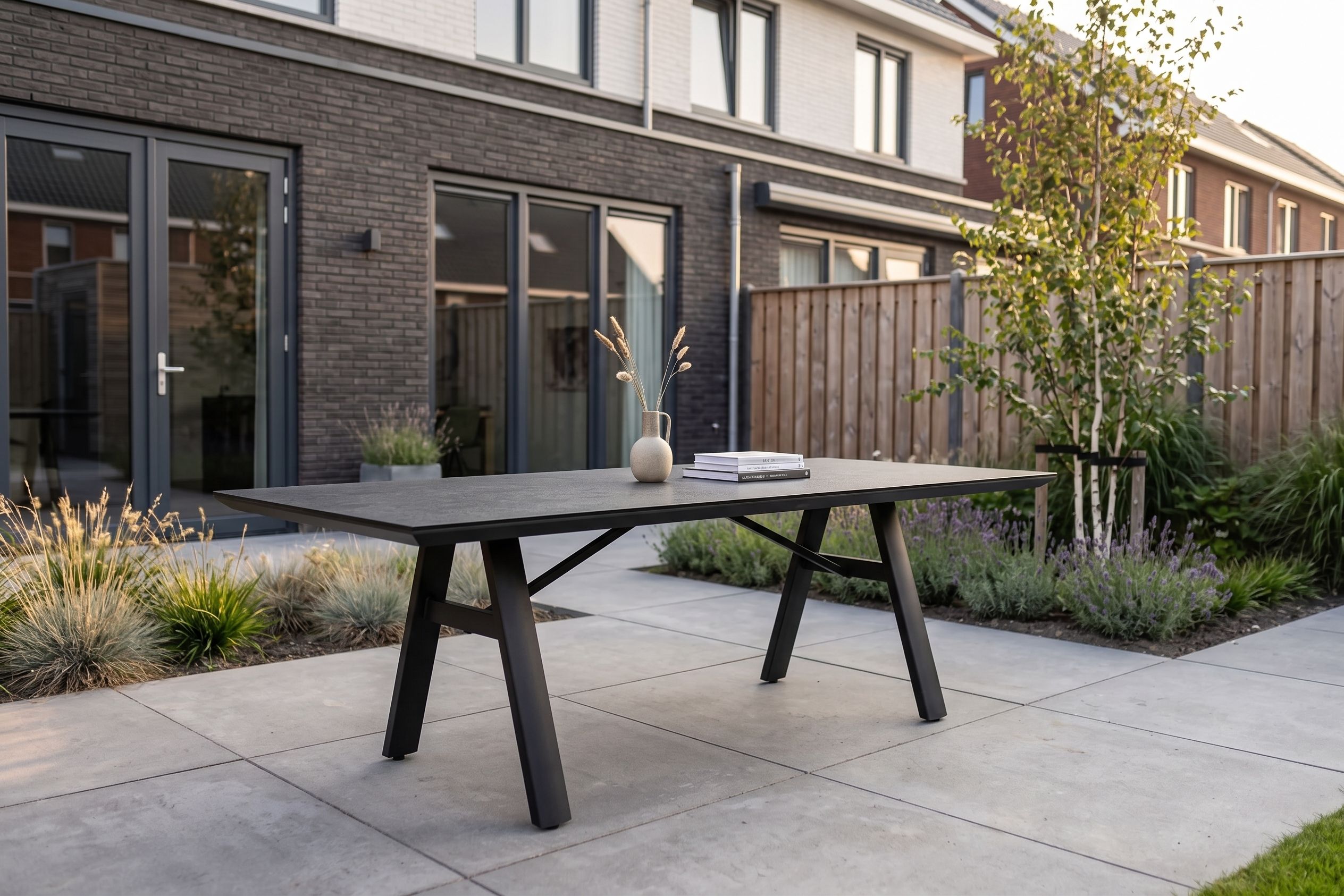 Moderne antracietgrijze tuintafel op een betegeld terras in een strak ingerichte achtertuin
