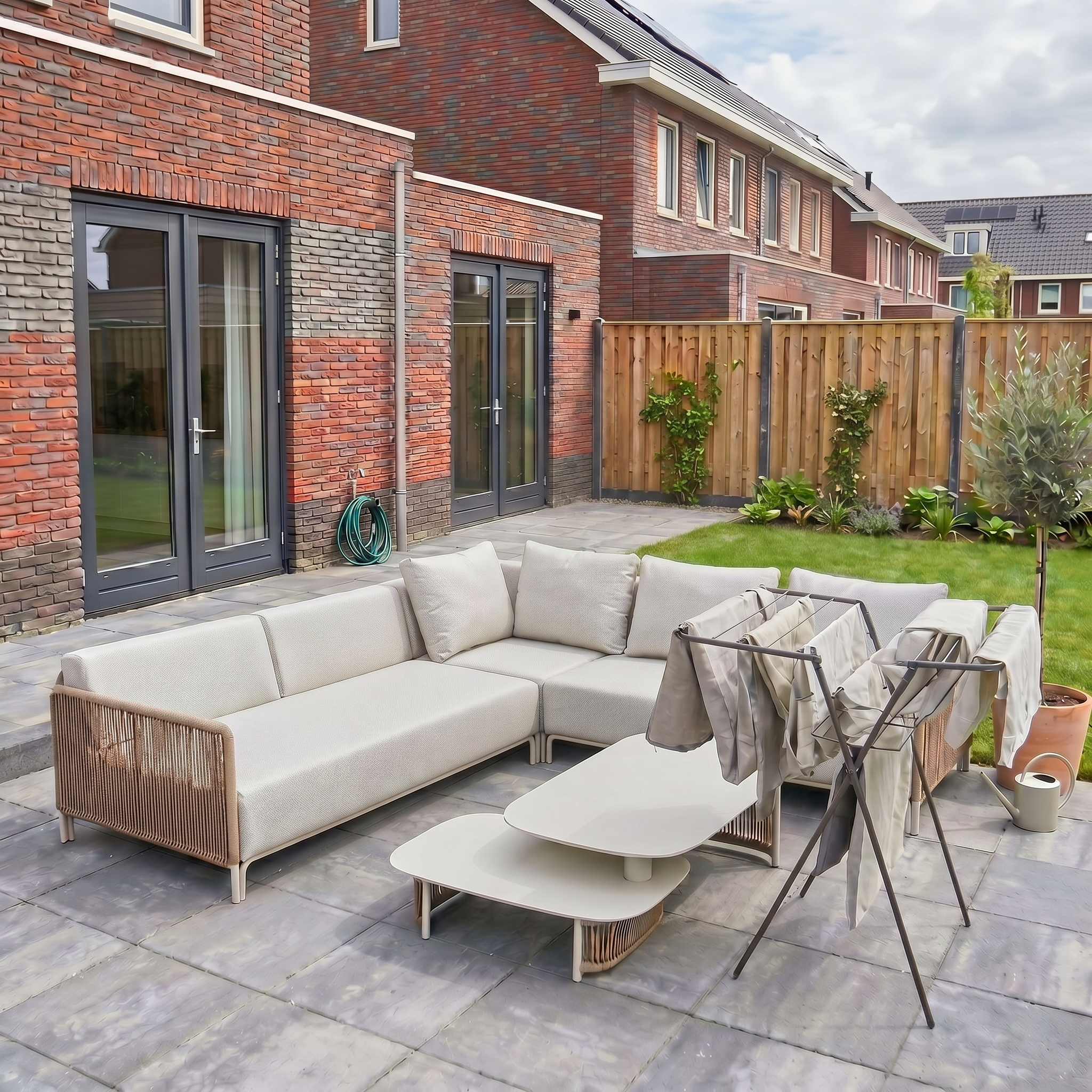Gewassen grijze kussenhoezen die hangend drogen op een wasrek in de achtertuin, naast de Ibiza stijl loungeset op een betegeld terras.