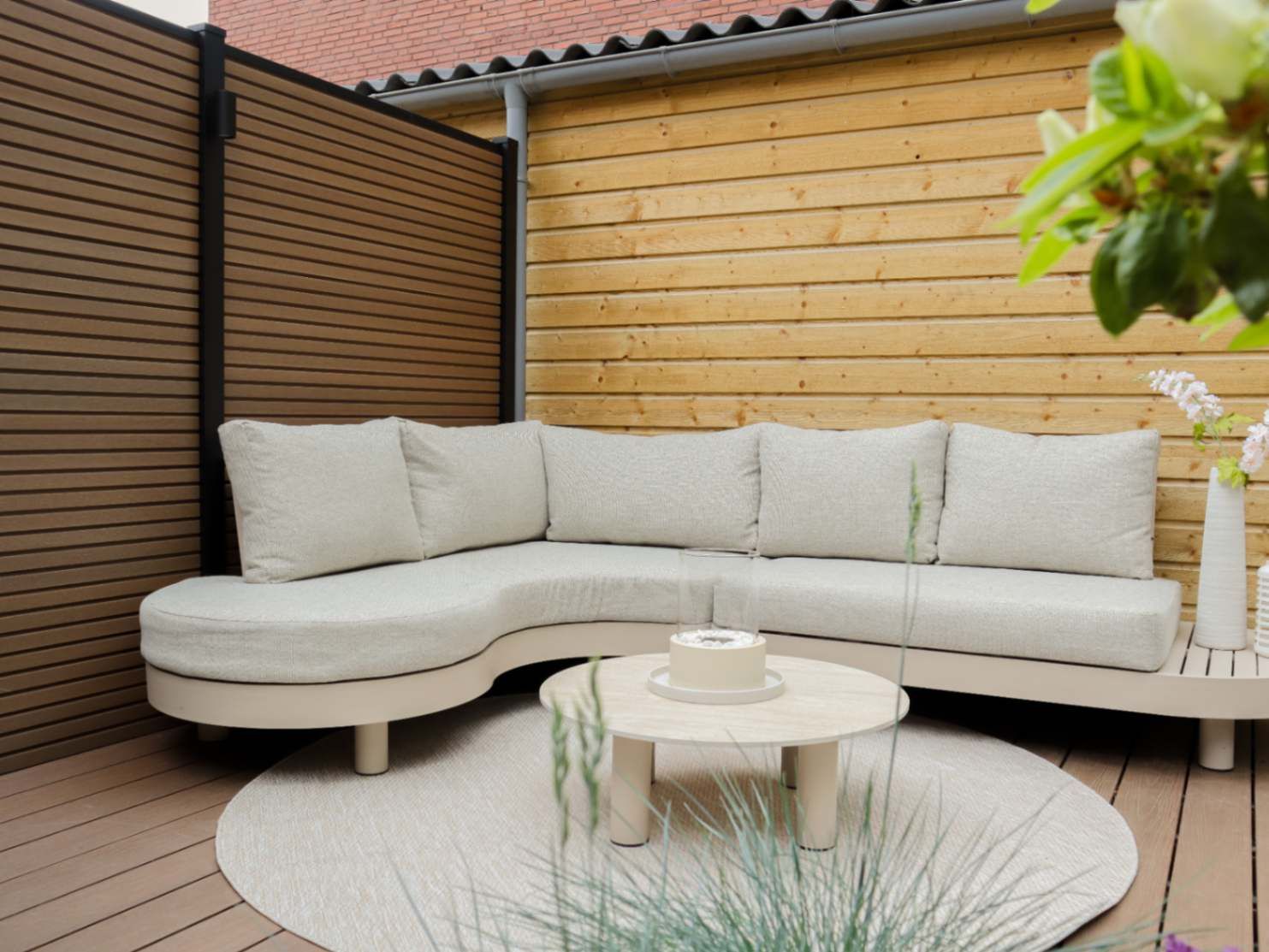 Beige hoekloungeset met ronde loungetafel op een houten vlonder