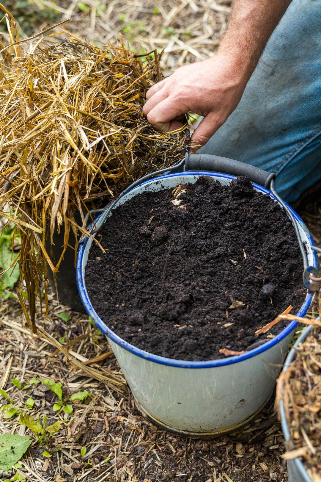 Emmer met compost naast stro voor de moestuin