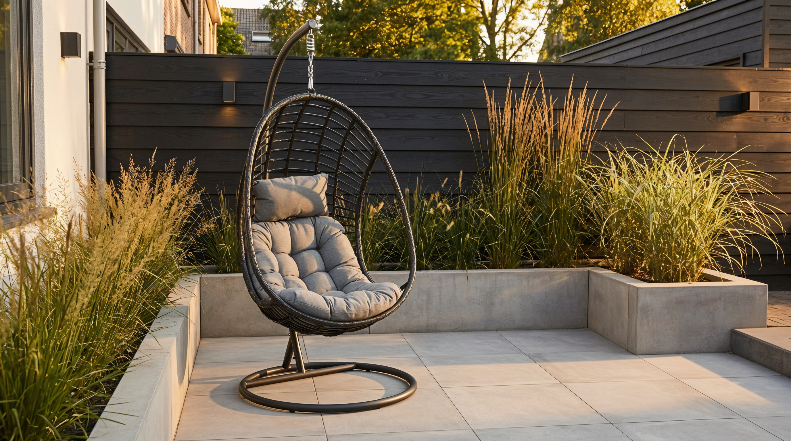 Hangende tuinstoel voor buiten met zwart frame en grijs kussen, geplaatst op een modern terras tijdens een zonnige herfstdag met warm licht.