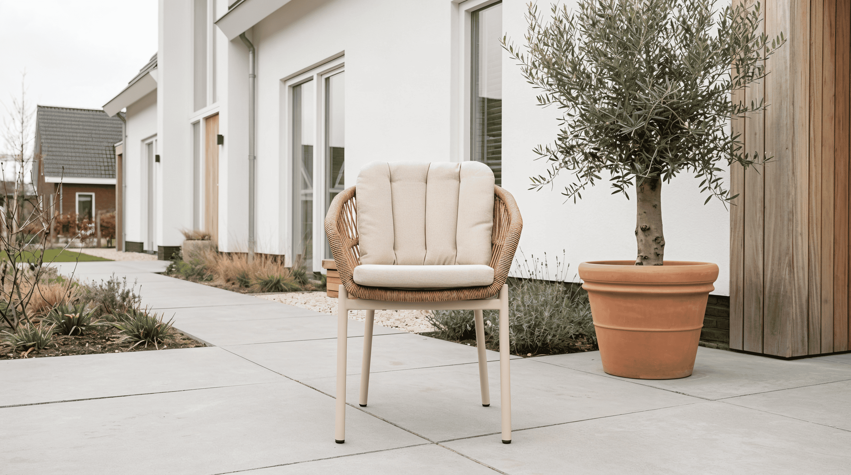 Comfortabele dining tuinstoel met ronde wicker rugleuning en licht zitkussen op een strak terras bij een moderne woning.