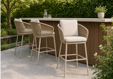 Stijlvolle rope diningstoelen met kussens rond een houten tuintafel op een terras met uitzicht op zee