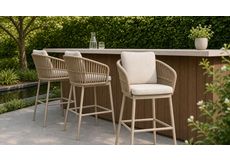 Stijlvolle rope diningstoelen met kussens rond een houten tuintafel op een terras met uitzicht op zee