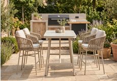 Koppel geniet van een drankje aan een moderne aluminium barset met hoge tuinstoelen en bartafel op een terras