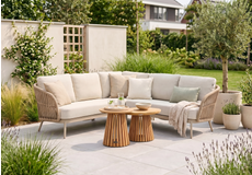 Moderne beige loungeset met hoekbank en ronde bijzettafels op een terras, stijlvolle wicker tuinset met kussens