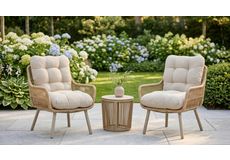 Set van twee luxe tuinstoelen met grijze kussens en blauwe sierkussens, naast een ronde wicker bijzettafel in een groene tuin