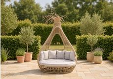 Ronde ligbed met grijze kussens en sierkussens op een groen gazon, luxe daybed voor in de tuin