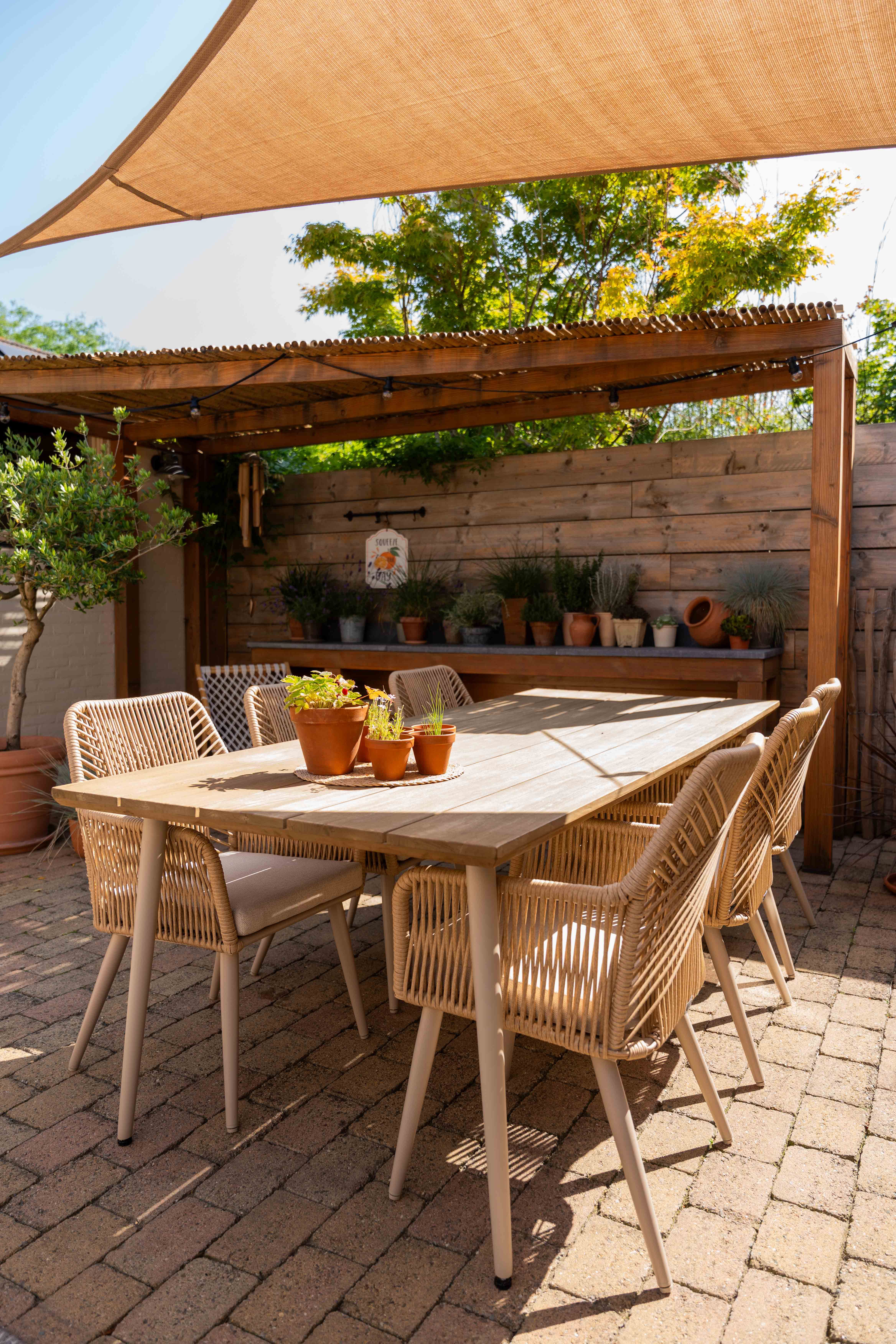 Vooraanzicht van een tuinkamer aan huis met een mediterrane tuinstijl, voorzien van een beige hoek loungeset en tuinset.