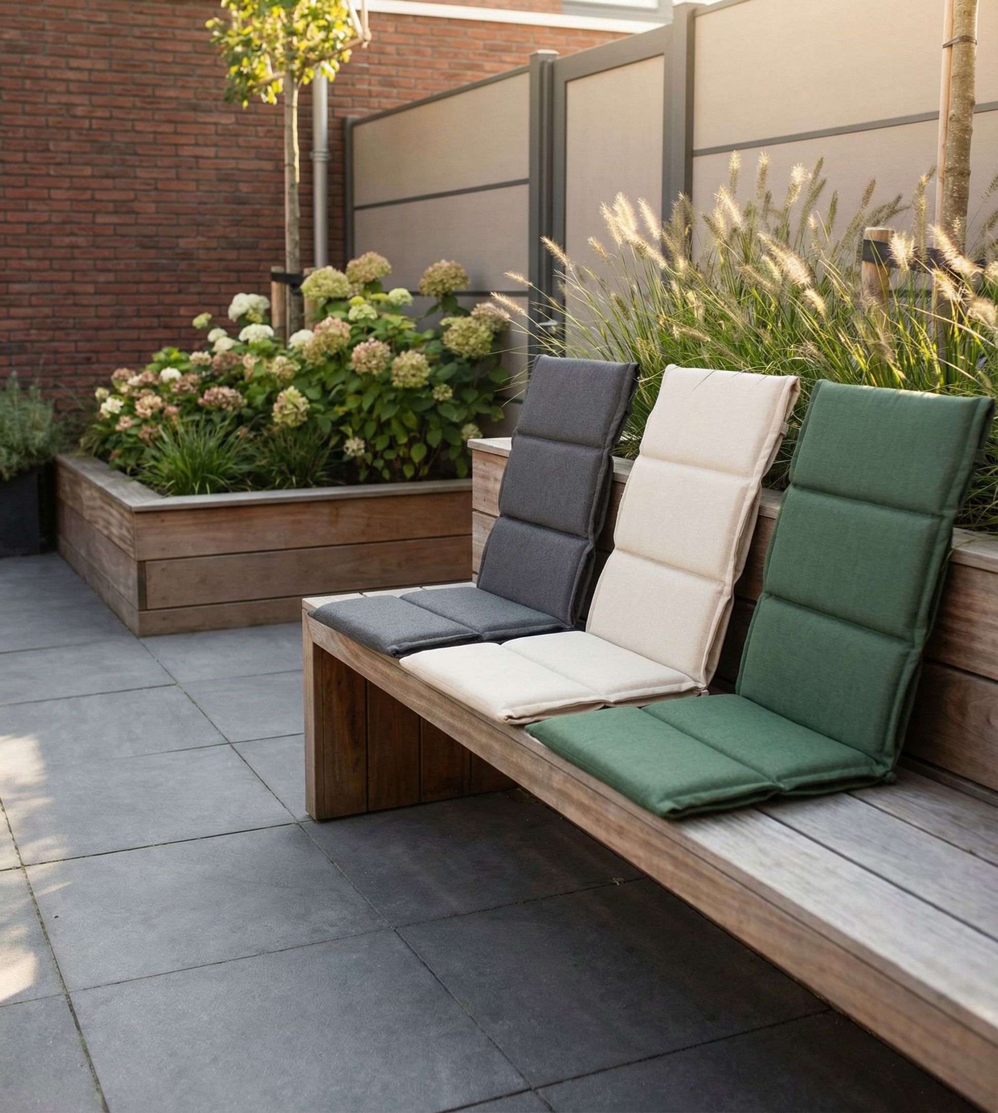 Drie verstelbare tuinstoelkussens in grijs, beige en groen op een houten tuinbank in een moderne, strak aangelegde tuin.