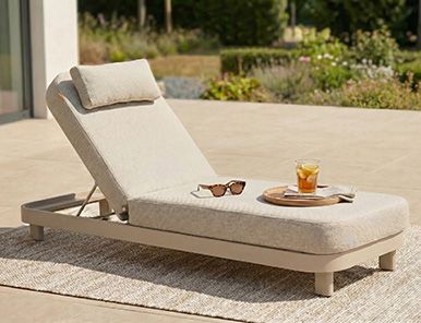 Vooraanzicht van een rond ligbed met grijze tuinkussens op een strak gazon bij een moderne woning met grote ramen.