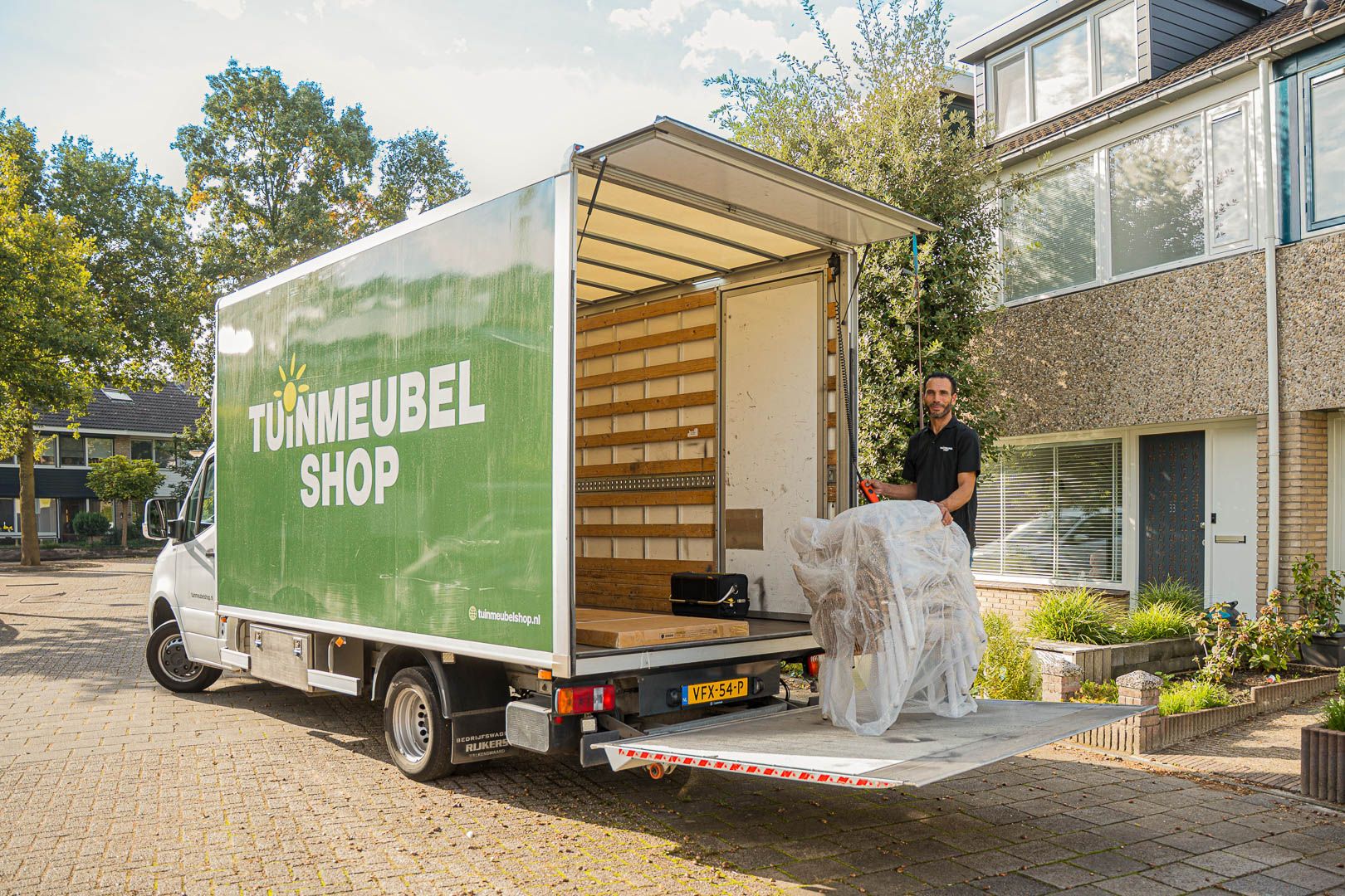 Bezorger van Tuinmeubelshop lost verpakte tuinmeubelen uit de vrachtwagen bij gratis bezorging aan huis.