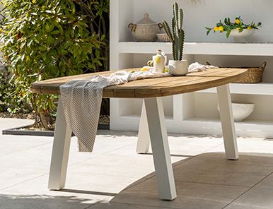 Vooraanzicht van een ronde houten tuintafel met verticale latten en vaasdecoratie in een japandi overkapping met glazen pui.
