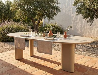 Vooraanzicht van een ronde houten tuintafel met verticale latten en vaasdecoratie in een japandi overkapping met glazen pui.