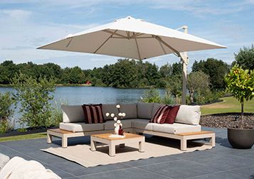 Achteraanzicht van een antracieten parasol naast een houten tuinset op een vlonderterras aan het water met groen landschap. 